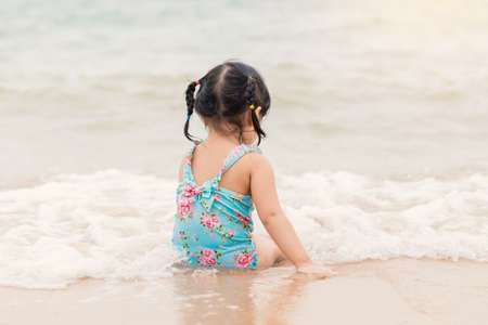 little girl sitting and playing on the beach with sand.の写真素材