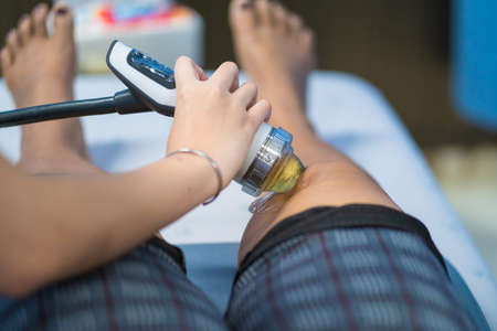 Therapist Doctor is doing shock wave therapy on Knee woman in hospital, Patient is getting Profilaxing Procedure of Physiotherapist. Health, Medicine.の写真素材