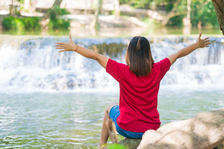 Young woman sitting on the root tree and enjoying waterfall landscape. Traveling nature near a beautiful waterfall at Chet Sao Noi waterfall National Parkの写真素材