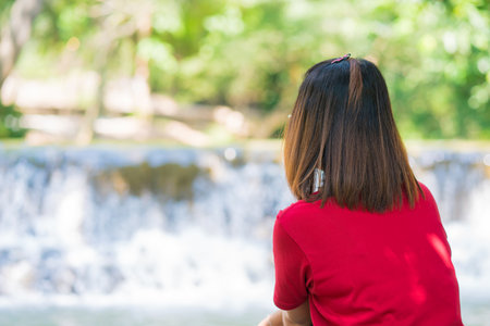 Young woman sitting on the root tree and enjoying waterfall landscape. Traveling nature near a beautiful waterfall at Chet Sao Noi waterfall National Park.の写真素材