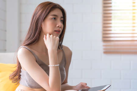 Asian woman relaxing sitting on sofa using smart phone at living room, Education technology and...