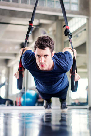 Sportsman or Handsome man doing exercise with fitness straps to strengthen his abdominal muscle in gym.の写真素材
