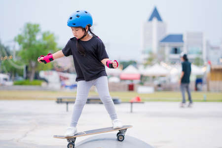 Child or kid girl playing surfskate or skateboard in skating rink or sports park at parking to...