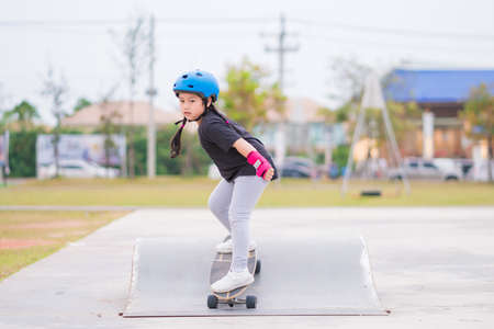 Child or kid girl playing surfskate or skateboard in skating rink or sports park at parking to wearing safety helmet elbow pads wrist and knee support.の写真素材
