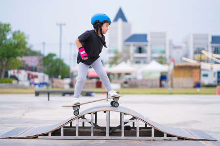 Child or kid girl playing surfskate or skateboard in skating rink or sports park at parking to wearing safety helmet elbow pads wrist and knee support.の写真素材