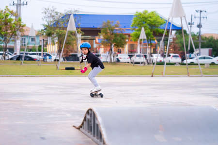 Child or kid girl playing surfskate or skateboard in skating rink or sports park at parking to wearing safety helmet elbow pads wrist and knee support.の写真素材