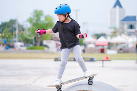 Child or kid girl playing surfskate or skateboard in skating rink or sports park at parking to wearing safety helmet elbow pads wrist and knee support.の写真素材