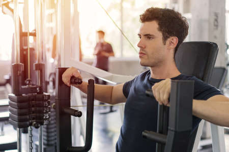 Handsome man lowering weight of fitness machine and working out in the fitness gym.の写真素材