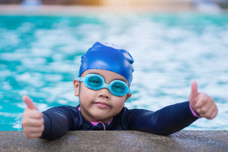 little girl smiling wearing swimming glasses in swimming pool. children playing in swimming pool on summerの写真素材