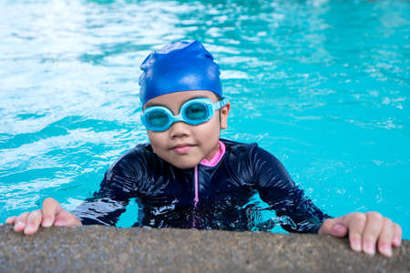 little girl smiling wearing swimming glasses in swimming pool. children playing in swimming pool on summer.の写真素材