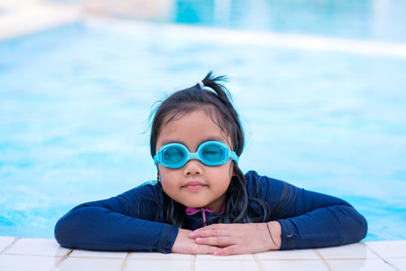 little girl smiling wearing swimming glasses in swimming pool. children playing in swimming pool on summerの写真素材