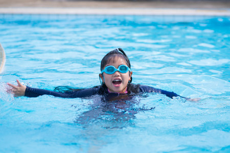 little girl smiling wearing swimming glasses in swimming pool. children playing in swimming pool on summer.の写真素材