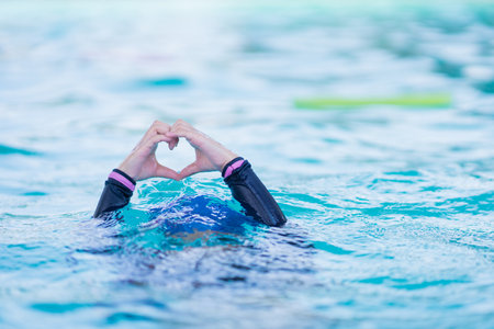 little girl wearing swimming glasses show hands in heart shaped under swimming pool. children playing in swimming pool on summer.の写真素材
