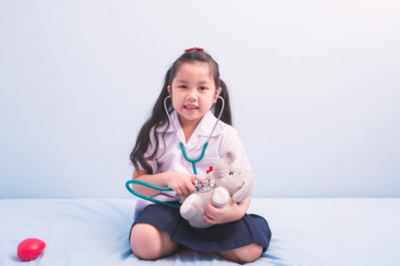 cute girls in medical uniform and stethoscope playing with a doll to be a doctor. child dreams of becoming a doctor career conceptの写真素材