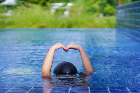 little girl wearing swimming glasses show hands in heart shaped under swimming pool. children playing in swimming pool on summer.の写真素材