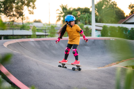 Child or kid girl playing surfskate or skateboard in skating rink or sports park at parking to wearing safety helmet elbow pads wrist and knee support.の写真素材