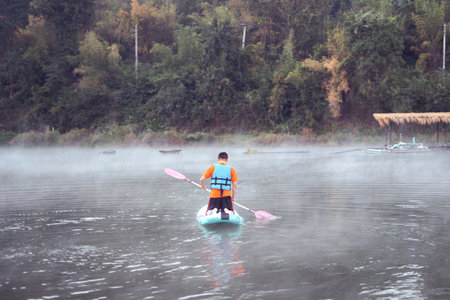 man on Paddleboard or sup board in middle of lake and enjoying sunrise and fog in the morning.の写真素材
