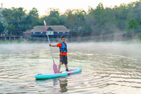 man on Paddleboard or sup board in middle of lake and enjoying sunrise and fog in the morning.の写真素材