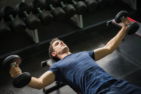 Handsome weightlifter lifting bench press working out with dumbbell in the gymの写真素材