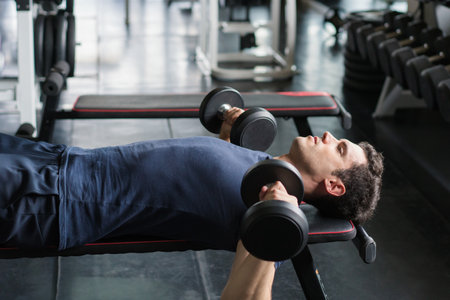 Handsome weightlifter lifting bench press working out with dumbbell in the gym.の写真素材