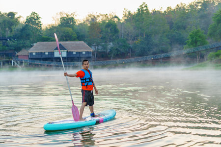 man on Paddleboard or sup board in middle of lake and enjoying sunrise and fog in the morning.の写真素材