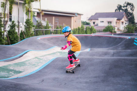 Child or kid girl playing surfskate or skateboard in skating rink or sports park at parking to wearing safety helmet elbow pads wrist and knee support.の写真素材