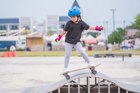 Child or kid girl playing surfskate or skateboard in skating rink or sports park at parking to wearing safety helmet elbow pads wrist and knee supportの写真素材