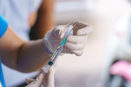 Doctor hands holding a vaccine bottle and syringe with needle filling with transparent fluidの写真素材
