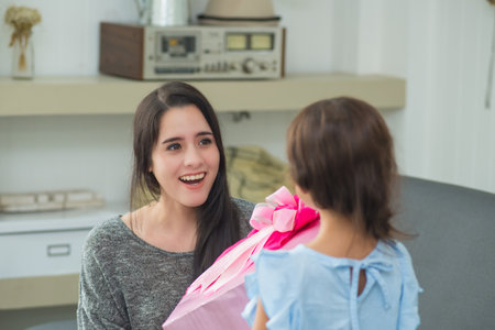 Beautiful young woman giving a gift box her sister on sofa in the living room at homeの写真素材