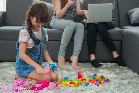 child a little girl is playing blocks at home. Mother with friend working on laptop or shopping online.の写真素材