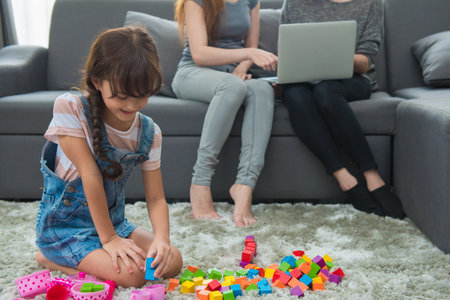 child a little girl is playing blocks at home. Mother with friend working on laptop or shopping online.の写真素材