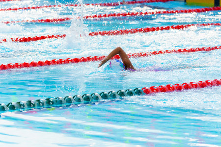 Swimmer child swims freestyle swimming style in a race swimming pool. Water sports and competition, learning to swim classes for children.の写真素材