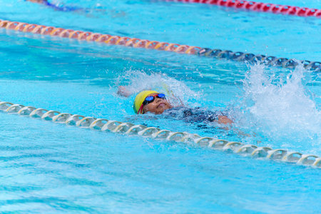 Swimmer child swims backstroke swimming style in a race swimming pool. Water sports and competition, learning to swim classes for children.の写真素材