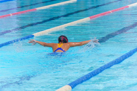 Swimmer child swims butterfly swimming style in a race swimming pool. Water sports and competition, learning to swim classes for children.の写真素材