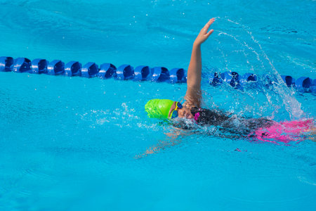 Swimmer child swims backstroke swimming style in a race swimming pool. Water sports and competition, learning to swim classes for children.の写真素材