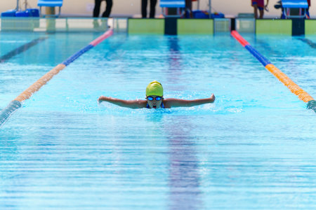 Swimmer child swims butterfly swimming style in a race swimming pool. Water sports and competition, learning to swim classes for children.の写真素材