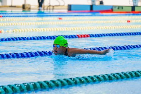 Swimmer child swims butterfly swimming style in a race swimming pool. Water sports and competition, learning to swim classes for children.の写真素材