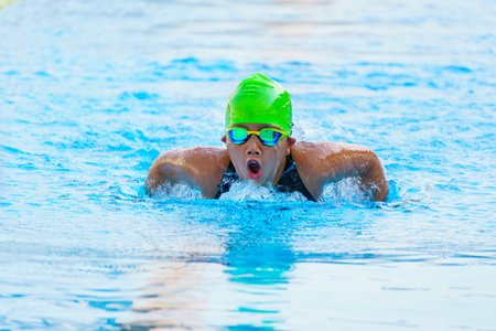 Swimmer child swims butterfly swimming style in a race swimming pool. Water sports and competition, learning to swim classes for children.の写真素材