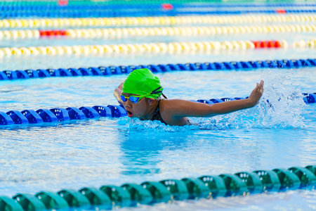 Swimmer child swims butterfly swimming style in a race swimming pool. Water sports and competition, learning to swim classes for children.の写真素材