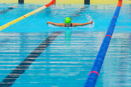 Swimmer child swims butterfly swimming style in a race swimming pool. Water sports and competition, learning to swim classes for children.の写真素材