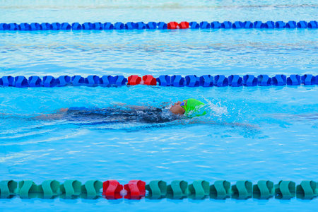 Swimmer child swims backstroke swimming style in a race swimming pool. Water sports and competition, learning to swim classes for children.の写真素材