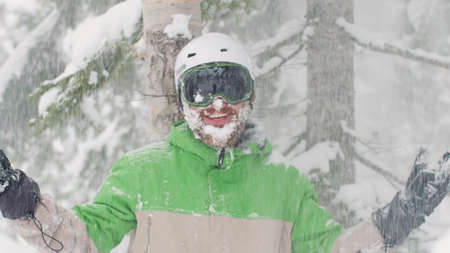 Large Amount of Snow Falling Off a Tree Onto Smiling Skier or Snowboarder Wearing a Helmet with Snowy Frozen Beardの写真素材
