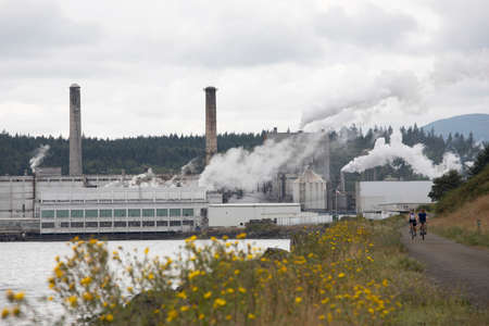 Port Townsend, Washington USA - August 2019: Cyclists Bike Down Pacific Northwest Larry Scott Trail Near Port Townsend Paper Corporation Mill Smoke Stacksの写真素材
