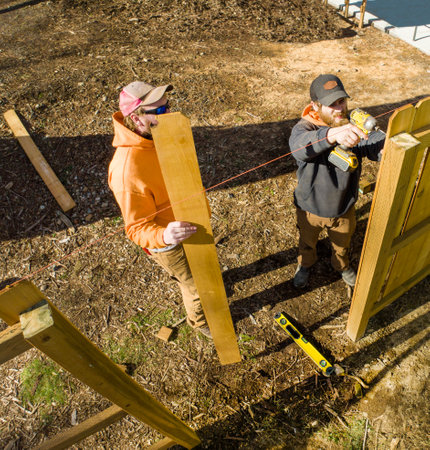 Contractors Working to Build a Fence With Wood Cedar Pickets Posts and Backer Railsの写真素材