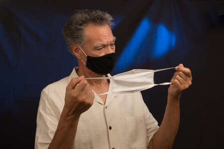 Senior man trying to decided what protective mask to wear the black one or white one