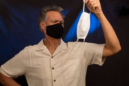Senior man trying to decided what protective mask to wear the black one or white oneの写真素材