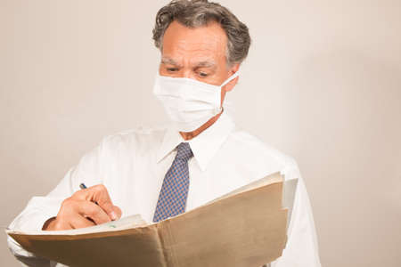 Doctor/Healthcare worker wearing a surgical mask checking over his patients reports