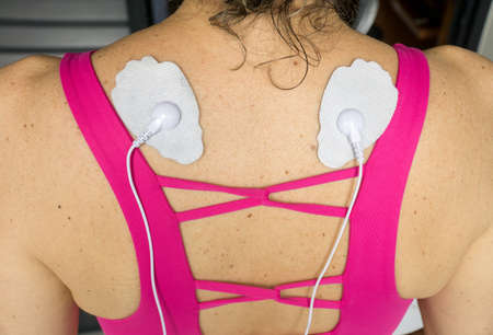 Woman using a Home Electrical Nerve Stimulation Unit also Known as TENS Unit on her Upper Backの写真素材