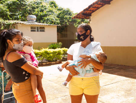 Planaltina, Goias, Brazil November 29 2020 : Two Young  women with their children wearing protective masks while waiting for food at a local feeding centerのeditorial素材
