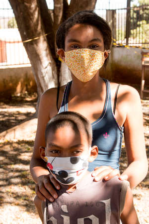Planaltina, Goias, Brazil-July 25 2020: A brother and sister wearing  protective masks while waiting for food at a distribution center for the poor of the communityのeditorial素材
